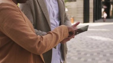  Tanınmayan iş adamı ve iş kadınının yavaş yavaş birlikte yürüdüğü orta bölüm takibi tabletteki bir şeye bakıyor.