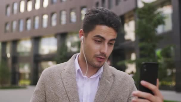 Sledování Záběr Pohledný Mladý Podnikatel Sluchátkách Drží Svůj Mobilní Telefon — Stock video