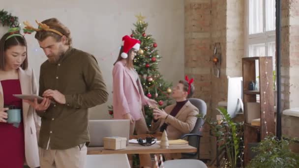 在Pan的照片中 商人们头戴喜庆的头巾 看着平板电脑 在办公室里聊天 然后摆姿势拍照 同事们在背景的圣诞树旁聊天 — 图库视频影像