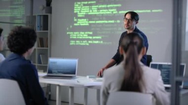 Bilgi teknolojileri öğretmeninin dizüstü bilgisayarlarıyla genç öğrencilerin önünde oturup ekran projektörüne atıfta bulunan kodlama programları hakkında konferans vermesi.