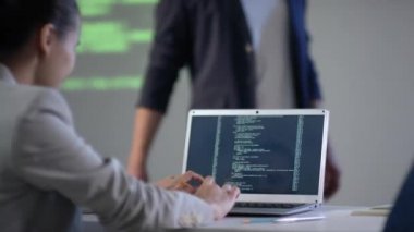 Bilgi teknolojileri dersinde dizüstü bilgisayarında yazı yazan genç ve melez bir kadın programcının yan görüntüsü. Öğretmen ileri geri konuşma yapıyor.