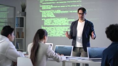 Genç erkek, bilgisayar programlama ve program kodlamasını arka planda ekran projektörü olan melez öğrencilerle tartışıyor.