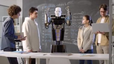 Genç öğrenciler ve bilişim profesörü arasında duran ve modern sınıflarda elleri yukarı aşağı hareket ettirme gibi beceriler gösteren etkin insansı robot.