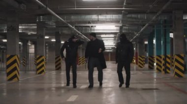 Deri ceketli üç eşkıyanın, suç üstüne karanlık otoparkı terk edişinin kar maskelerini çıkartıp tartışmalarını ve el kol hareketlerini ön cepheden çekimleri.