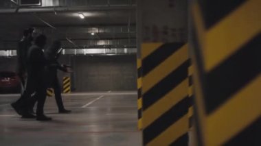 Çok ırklı bir grup silahlı suçlunun tecrit edilmiş yeraltı otoparkında suç mahallinden kaçışının tam bir yan görüntüsü.