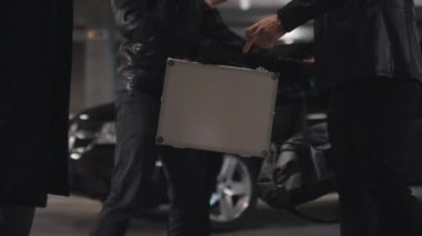 Gizli otoparkta yasadışı anlaşma yapan silahlı suçluların yasak eşyalar karşılığında para alışverişinde bulunduğu orta bölüm görüntüleri.