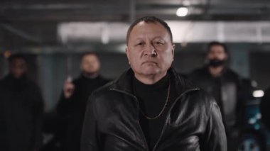 Asyalı mafya liderinin orta ölçekli yakın çekimi. Kameraya bakıyor. Elinde tabancalar var.