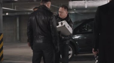 İki çoklu etnik suç çetesinin yeraltı otoparkında buluşması ve liderlerin uyuşturucu liderinin kontrol için bir paket aldığı metal evrak çantası göndermesi.