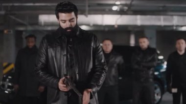 Arka planda siyah arabanın yanında duran çok ırklı haydut çetesiyle kameraya bakarken Orta Doğulu sakallı bir suçlunun portresi.