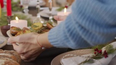 Kadın elinin PAN 'ı, kavrulmuş patates ve biberiye ile birlikte yanan mumlar ve çam dallarıyla süslenmiş Noel sofrasına koyuyor.