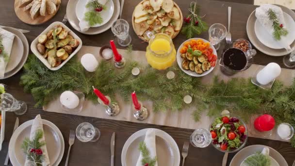 様々なおいしい料理とキャンドルや松の枝から作られた中心部で飾られたクリスマステーブルのトップビューの追跡 — ストック動画