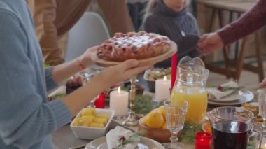 Kadın elinin PAN orta kesimi, tanınmayan bir kadına ahşap tabakta lezzetli turtalar sunarken Noel 'de yemek masasının hazırlanmasına yardım ediyor.