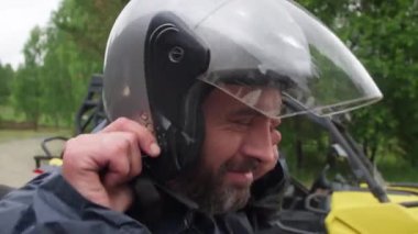 Ciddi orta yaşlı, sakallı, kaskını takan ve dışarıda bisiklete binmeden önce kayışlarını bağlayan bir adama yakın durun.