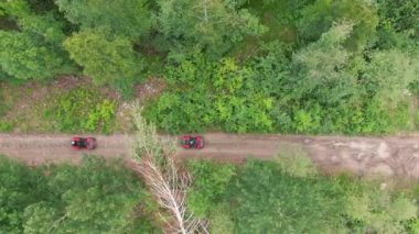 Dar orman yolu boyunca çamur ve su birikintilerinde kırmızı dörtlü bisiklete binen insanların çekimleri.