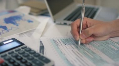 Tanımlanamayan kadın el yazısını yazılı vergi iadesi formunda kapatın. Bilgileri bulanık dizüstü bilgisayar ve arka plandaki kağıtlarla tamamlayın.