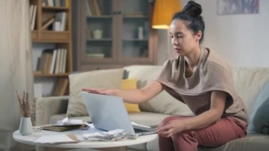Genç melez kadının oturma odasında dizüstü bilgisayarını açıp bütçe yönetimi için yığınla fatura ve çek aldığı orta boy görüntüler.