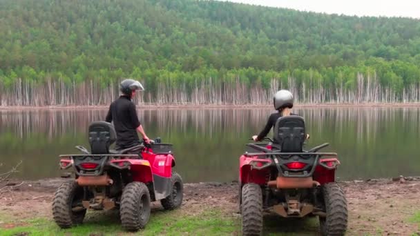 美しいエリアの湖で赤いクワッドバイクに座ってヘルメットでカップルの空中ショット — ストック動画