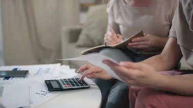 Karışık ırktan genç bir kadının faturaları saymasına yardım ettiği ve evde oturup hesap makinesi kullanarak aylık tutulan kağıtları analiz ettiği görüntüler.