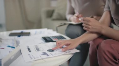 Aile bütçesinin daha iyi yönetilmesi için basılı diyagramlar ve çizelgelerle dolu kahve masasının kapatılması ve tanınmayan bir kadının parmaklarının yazılı bilgileri kontrol etmesi