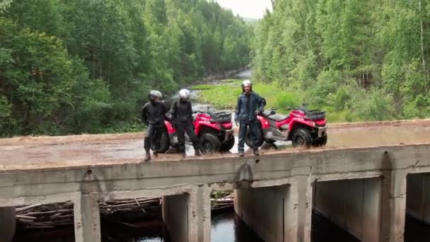三个戴钢盔骑四轮驱动自行车的人站在森林桥上欣赏风景的空中镜头 — 图库视频影像