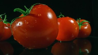 Bahçeden toplanan ıslak kırmızı domateslerin siyah cam yüzeydeki makro görüntülerini tarıyorum.