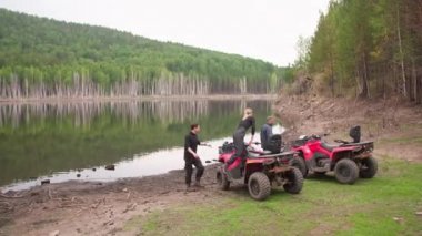 Ormandaki gölün kenarında dinlendikten sonra kırmızı dört tekerlekli bisiklete binip miğferlerini takan kadın ve erkeklerin uzak plan fotoğrafları.