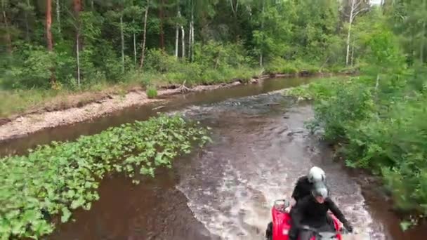 男男女女戴着头盔驾驶红色越野车在森林中驶过河流 — 图库视频影像