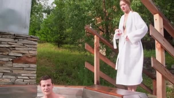 手持追踪器追踪年轻女子脱下浴袍 与男友和朋友一起在室外热水浴缸里 — 图库视频影像