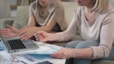 Sehpada oturan kadınların mali ve iş konularında danışmanlık yaptığı, vergi beyannamesini doldurduğu ve dizüstü bilgisayara veri girdiği orta bölüm görüntüleri.