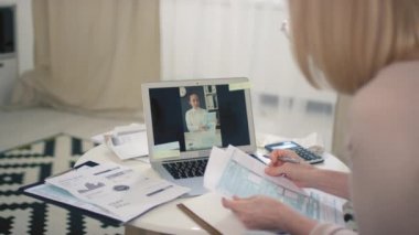 Orta yaşlı beyaz bir kadının finans danışmanıyla görüntülü konuşma yaparken ve diyagramları tartışırken çekilmiş görüntüler.