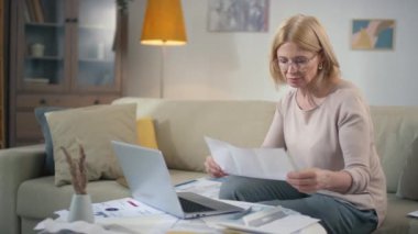 Orta yaşlı, beyaz bir kadının faturaları ve ödemeleri kontrol ederken mali kayıp ve krizle ilgili hayal kırıklığına uğradığı orta büyüklükte görüntüler.