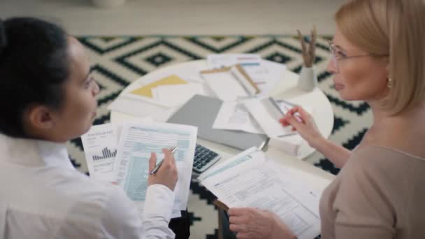 穿着白衬衫的银行职员帮助中年妇女填写坐在明亮客厅沙发上的纳税申报单的俯瞰镜头 — 图库视频影像