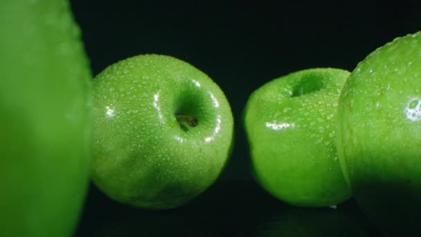 ズームアウトゆっくりマクロまだ人生ショットの4つの滑らかな熟した緑のリンゴとともに水滴がスタジオで暗い表面上に横に横たわっている — ストック動画