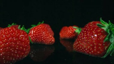 Tatlı yaz çileklerinin makro görüntülerinde oynaşmak stüdyodaki parlak, karanlık yüzeye yeni toplanmış ve yıkanmış.