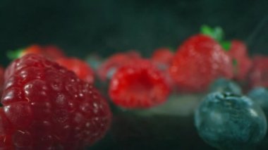 İzole edilmiş taze çilek, ahududu ve yaban mersinlerinin koyu renkli yüzeyde dumanlı görüntüsü.