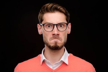 Kirli sakallı, siyah arka planda duran gözlük takan kendinden geçmiş bir gencin portresi.