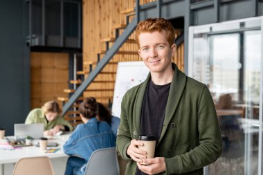 Genç başarılı ofis müdürü kameranın önünde içki içiyor ve iş arkadaşlarının toplantı yapmasına karşı sana bakıyor.