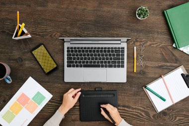 Çağdaş yaratıcı tasarımcının elleri dizüstü bilgisayarın önündeki ahşap masada oturuyor ve stil ve grafik tablet kullanıyor.