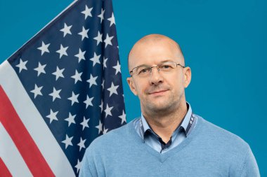 Gözlüklü, mavi kazaklı orta yaşlı, kendinden emin bir avukat ya da işadamı kameranın önünde dikilirken sana bakıyor.