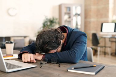 Formalite icabı fazla çalışan genç iş adamı ofis ortamında çalışırken dizüstü bilgisayarın önünde uyukluyor.