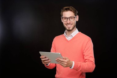 Gülümseyen, sakallı, parlak kazaklı genç adam izole edilmiş arka planda sosyal medyada dijital tablette sörf yapıyor.