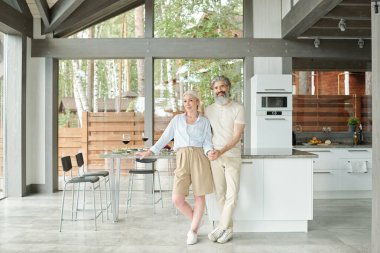 Modern evde mutfağa sarılan gülümseyen yaşlı çiftin portresi.