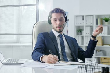 Masada oturan tatmin olmuş genç analist ofiste belgelerle çalışıyor.