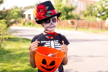 Siyah cadılar bayramı tişörtlü ve şık şapkalı, elinde plastik sepetli kır evlerindeki insanların verdiği şekerlerle boyalı çocuk.