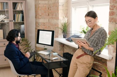 Genç bayan mobil uygulama geliştiricisi dijital tablette kaydırırken erkek arkadaşı da bilgisayar ekranının önünde robot resimlerle oturuyor.