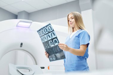 Hasta hastane odasında uyurken, cerrahi maskeli düşünceli doktor ve hemşire röntgen görüntülerini analiz ediyor.