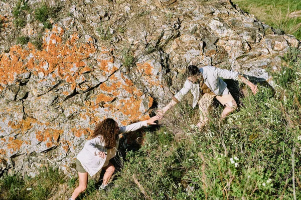 年轻的徒步旅行者向女朋友伸出手来 在探险时帮助她攀登悬崖 — 图库照片