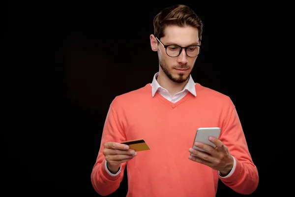 クレジットカード残高を確認しながらスマートフォンアプリを使用して眼鏡でハンサムな若い男の笑顔の肖像画 — ストック写真