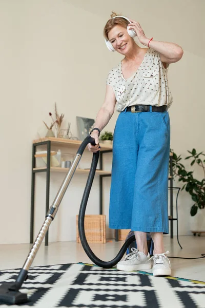 Cheerful Mature Housewife Casualwear Listening Music Headphones While Cleaning Carpet — Stock Photo, Image