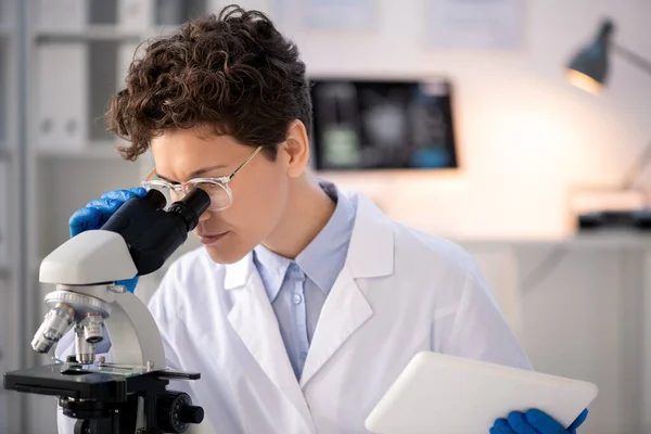 Joven Científica Seria Whitecoat Guantes Mirando Microscopio Mientras Usa Touchpad — Foto de Stock